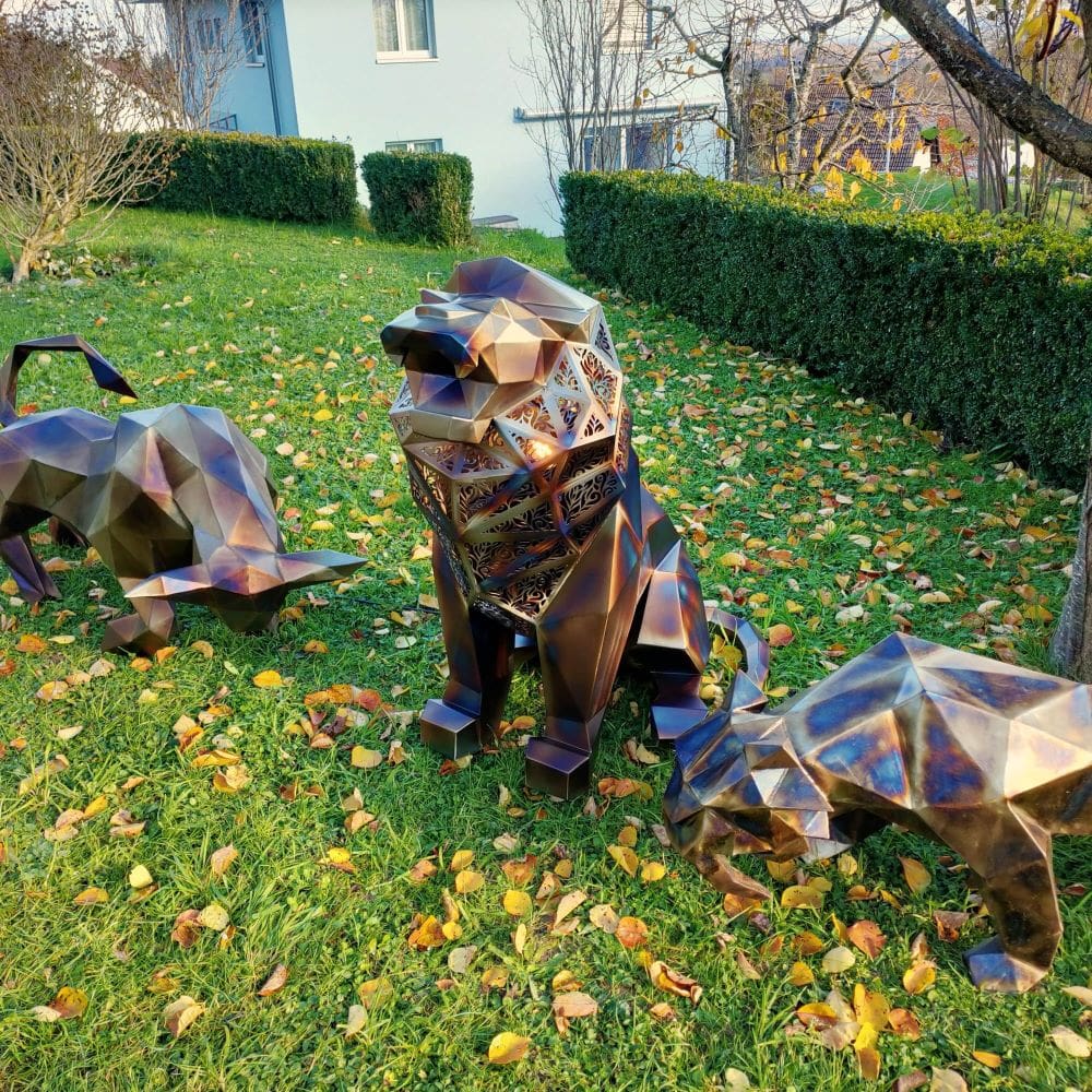 Group of custom polygonal lion sculptures crafted in multicolor welded steel, showcased on green grass